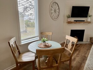 A dining area with a round table, four wooden chairs, a potted plant, a wall-mounted TV, and a fireplace. - Flash Sale Completely updated 3/2 Sleeps 8 ML19 (Orange Beach)