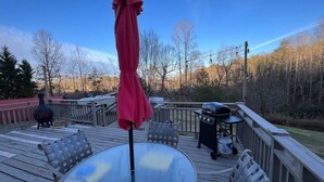 Eine Terrasse mit einem Glastisch, Metallstühlen, einem roten Sonnenschirm und einem Grill.