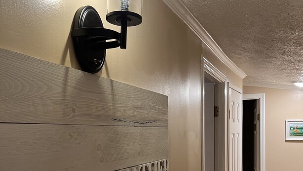 Ein Korridor mit einem an der Wand befestigten Holzschild, das „GATHER Hier mit dankbaren Herzen“ besagt, und einer Wandleuchte darüber.