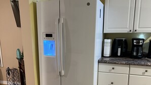 Eine Küche mit einem weißen Kühlschrank, weißen Schränken, einer Kaffeemaschine und einem Wasserkocher auf der Arbeitsfläche.
