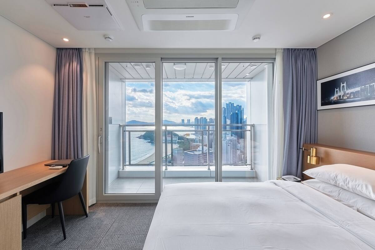 A hotel room with a large sliding glass door leading to a balcony with a city view.