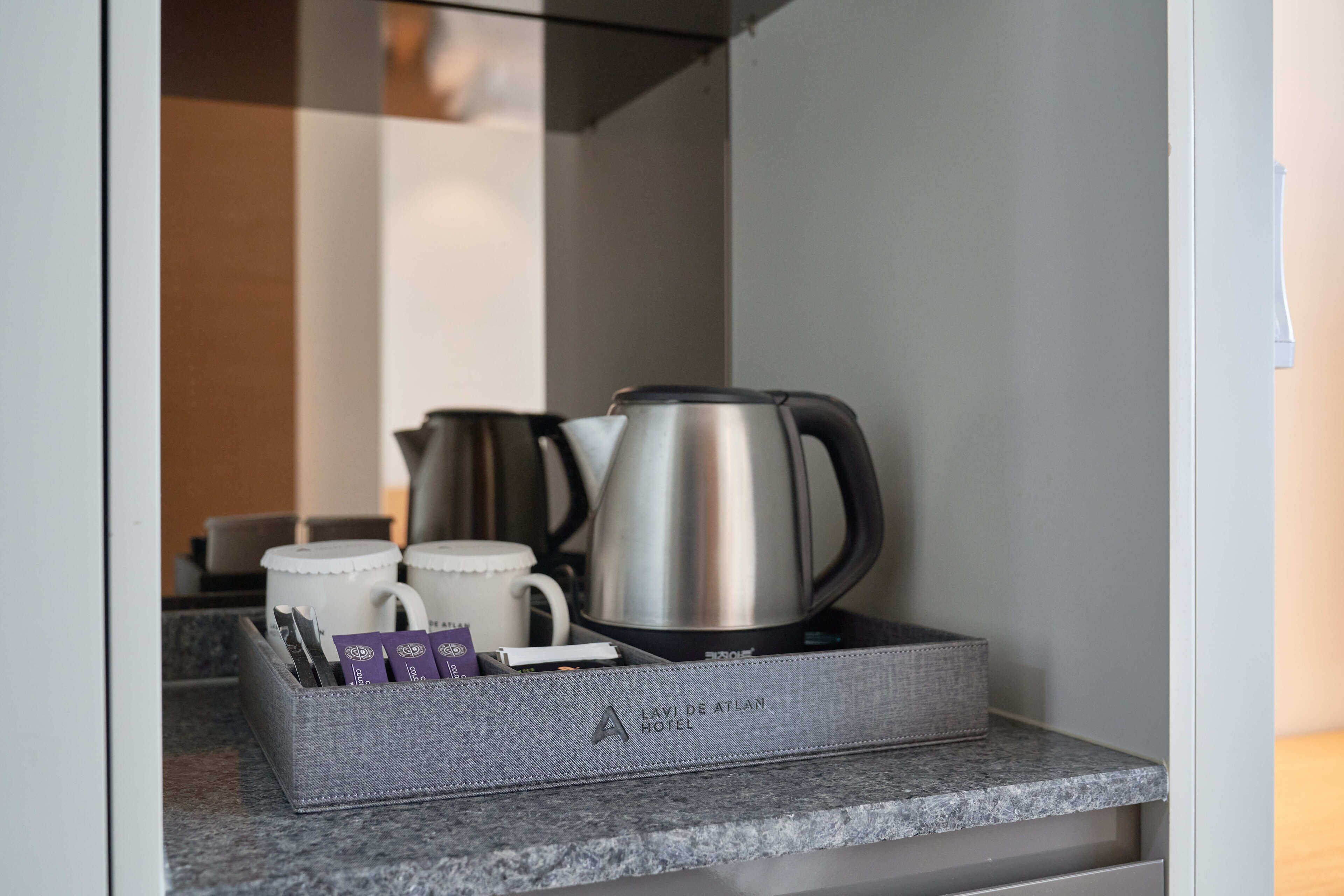 A kitchen counter with a kettle, two white mugs, and a tray with cards.