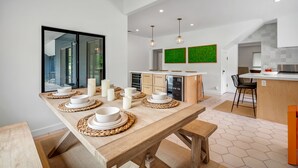 Uma cozinha moderna com mesa de madeira posta para refeições, uma janela grande e uma parede verde.