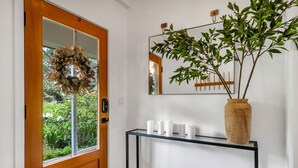 Uma porta de madeira com um painel de vidro, uma coroa de flores e um console com velas e uma planta em vaso.