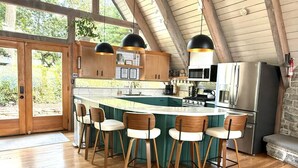A modern kitchen with a large island, bar stools, and a stone fireplace. - A-frame W/ Hot-tub, Mountain View & tennis court (Newport)