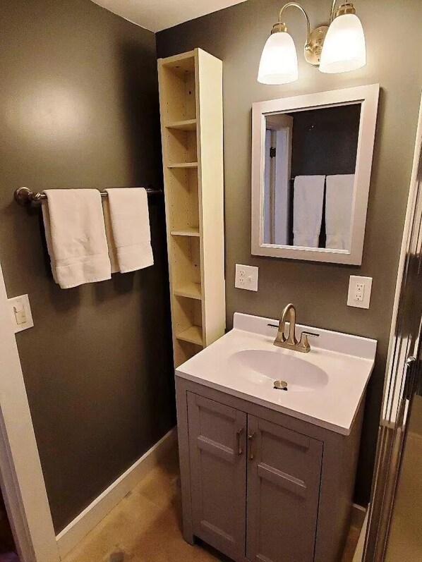 Un baño con un lavamanos blanco, dos toalleros, un espejo y una estantería.