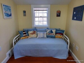 Cozy bedroom with a single bed, nautical-themed pillows, and a window with blinds.