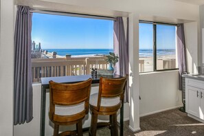A balcony with a table and chairs, overlooking a beach and ocean.