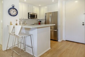 A modern kitchen with white cabinetry, stainless steel appliances, a bar stool, and a wall clock.