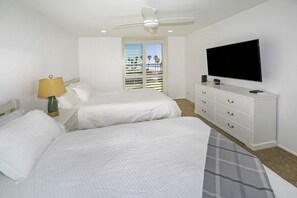 A hotel room with two beds, a ceiling fan, a TV, and a window with blinds.