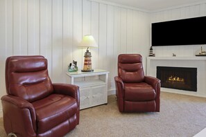 A living room with two leather armchairs, a white sideboard with a lamp, and a fireplace with a TV mounted above it.