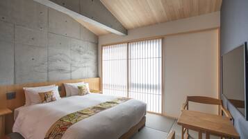 A modern bedroom with a large bed, a wooden headboard, a small table, and a TV on the wall.