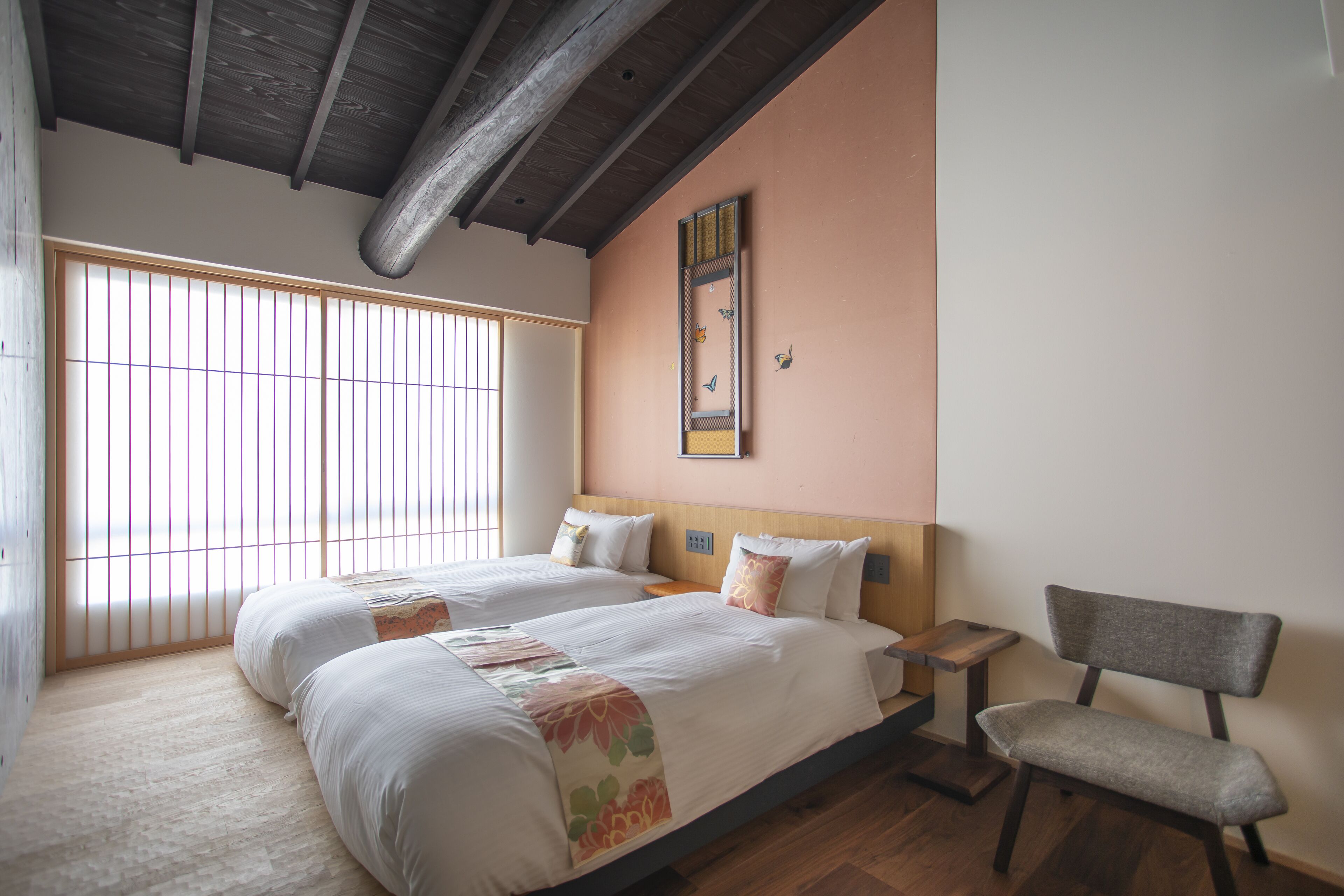 Une chambre avec deux lits, des poutres en bois au plafond, une grande fenêtre et un fauteuil.