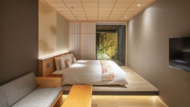 Quarto moderno com cama, um banco e vista para um jardim.