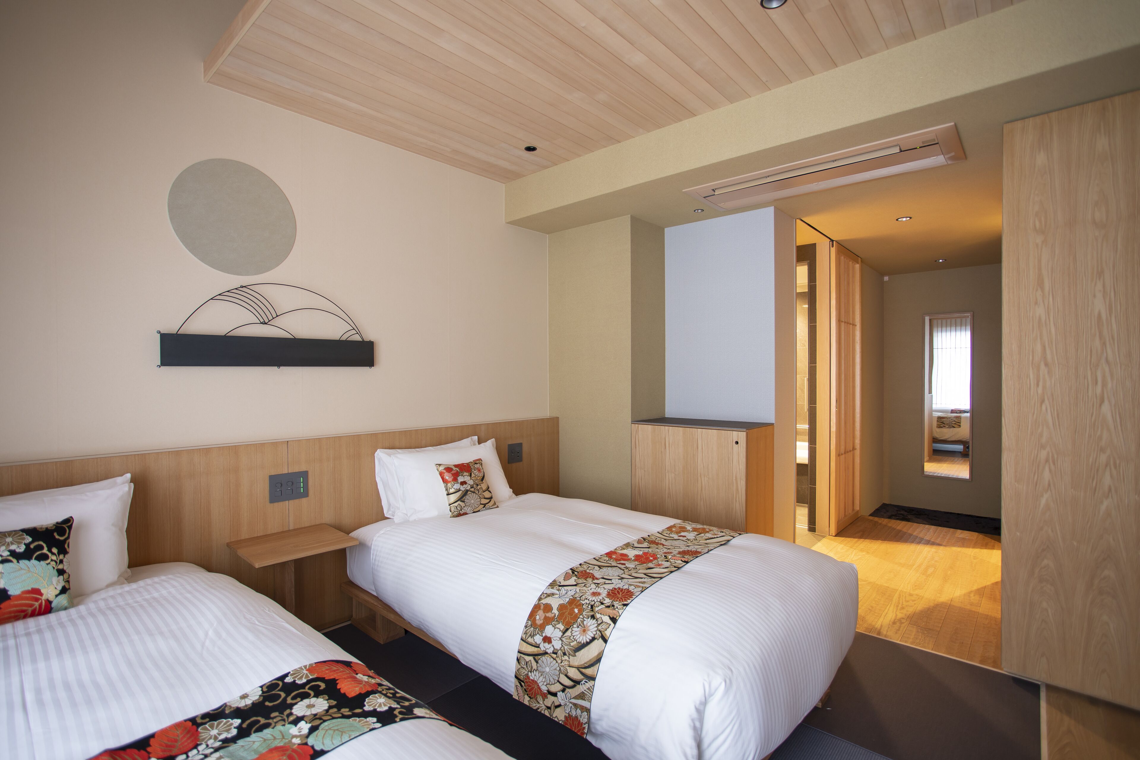 A hotel room with two beds, a wooden ceiling, a wall-mounted TV, and a large mirror.
