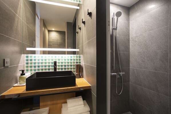 Un baño moderno con un espejo grande, un lavabo negro, ducha y encimera de madera.