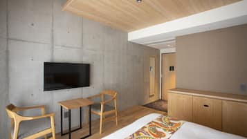 A modern hotel room with a large bed, a flat-screen TV mounted on the wall, wooden furniture, and a ceiling with wooden beams.