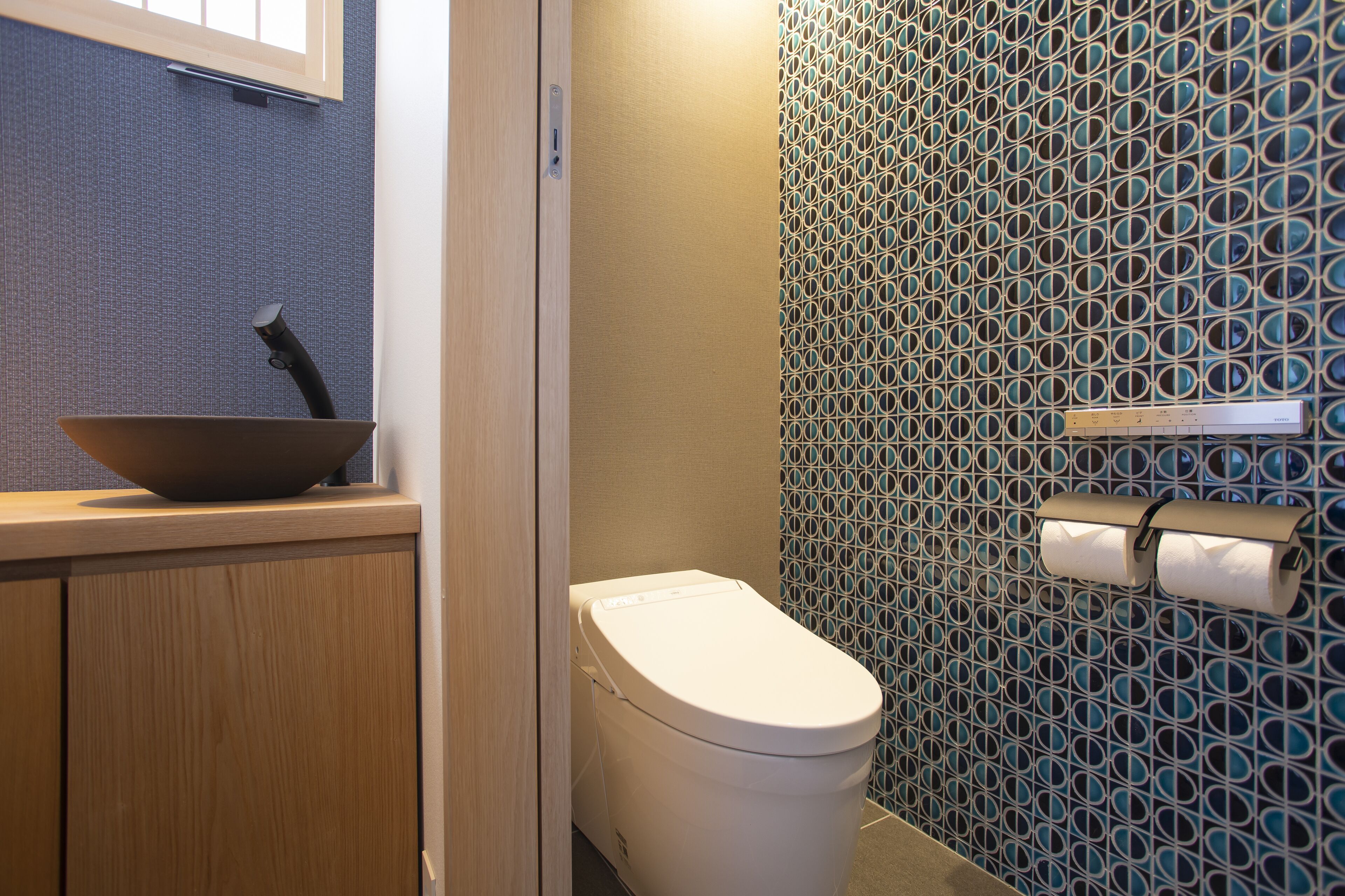 A bathroom with a toilet, a sink with a bowl, and a patterned wall.