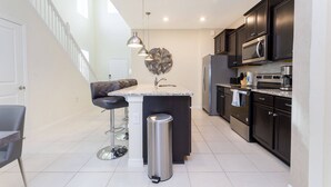 A modern kitchen with dark cabinets, a stainless steel refrigerator, a microwave, and a granite countertop island with bar stools. - Beautiful 6 Bedroom Home w/ Private Pool and Spa at Windsor Island (Davenport)