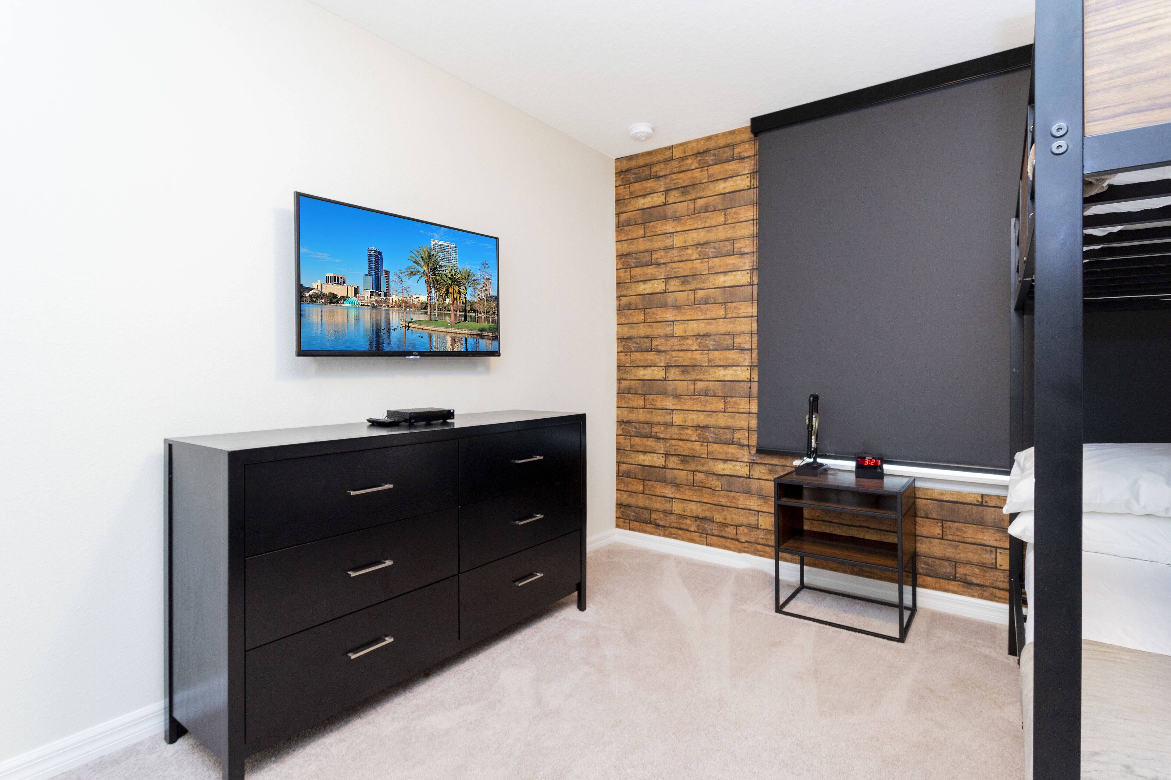 Een moderne slaapkamer met een zwarte dressoir, een aan de muur bevestigde televisie, een accentmuur van baksteen, en een bed met een zwart hoofdeinde.