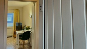 Une chambre d’hôtel avec un plancher en bois, un coin repas avec une table et des chaises, une télévision et une fenêtre avec des rideaux.
