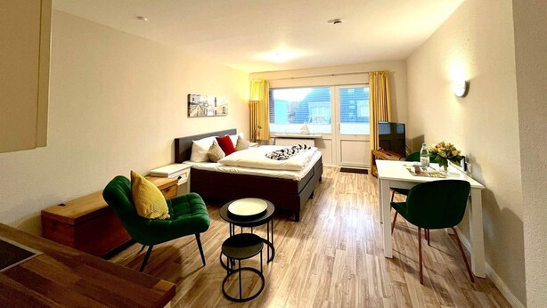 Une chambre d’hôtel de taille modeste, comprenant un lit, un bureau, deux chaises, une petite table et une fenêtre avec des rideaux.