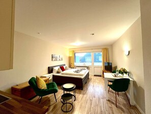 A compact hotel room with a bed, a desk, two chairs, a small table, and a window with curtains. - Mare Nostrum 7 Vacation Apartment—close to the beach, close to town, close to relaxation—in short— (Sylt)