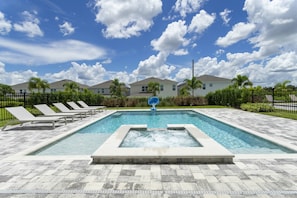 Piscina com espreguiçadeiras, hidromassagem e vista para casas ao fundo.