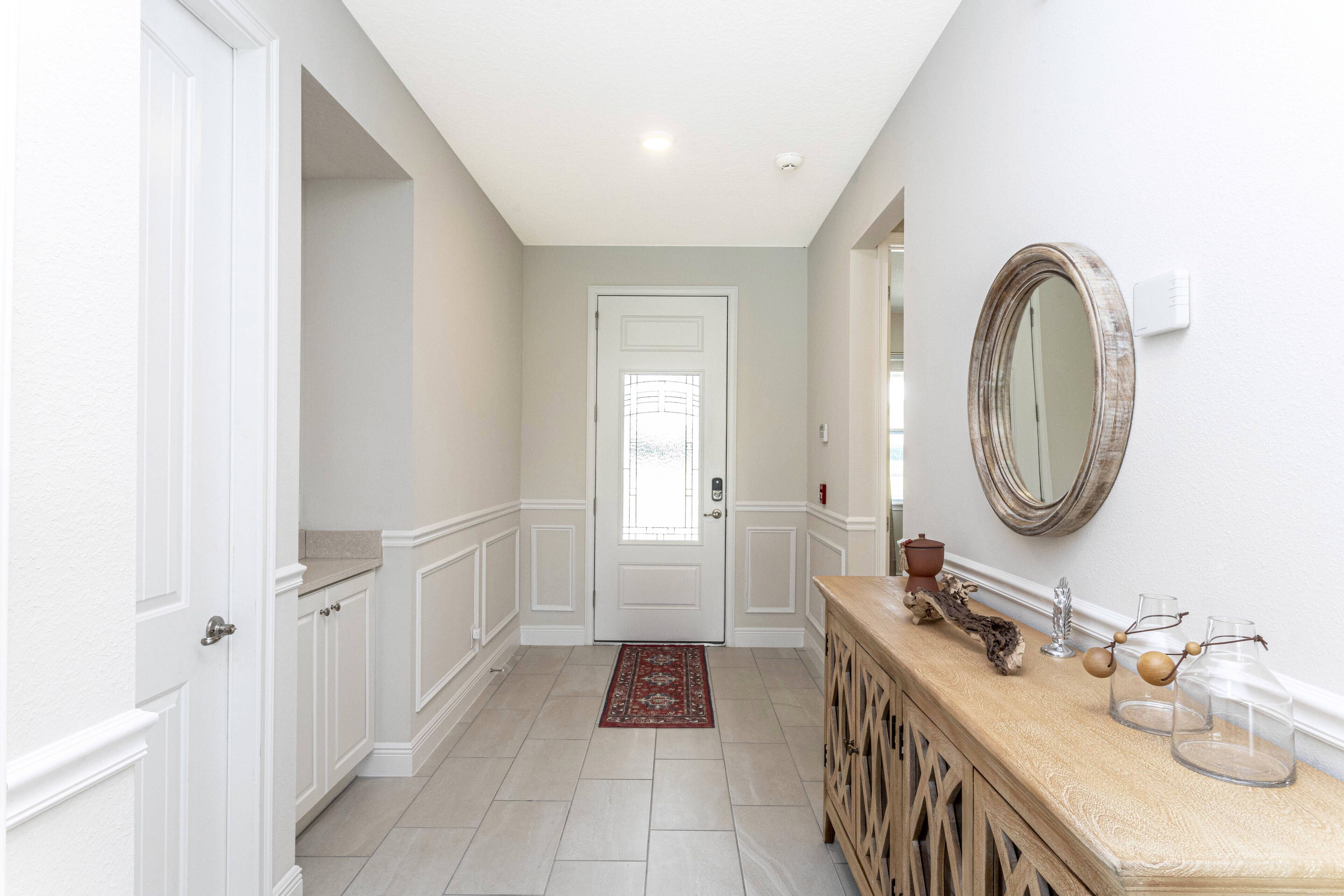 A hallway with a white door, a wooden console table with decorative items, and a mirror on the wall.