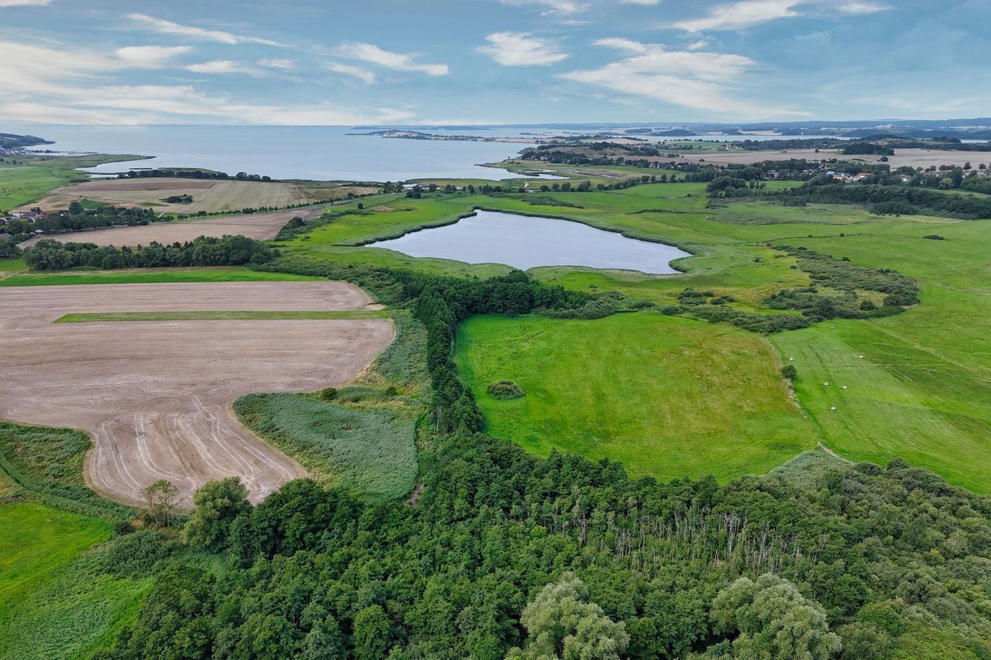 Eine Vogelperspektive auf eine ländliche Landschaft mit Feldern, einem See und einem bewaldeten Gebiet.