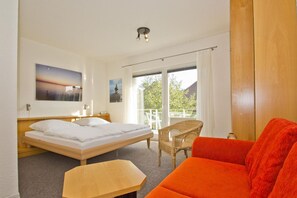 A hotel room with a bed, a wooden table, a wicker chair, and a red sofa. - Only 100 m to the beach, apartment with balcony and terrace - App. Eldena FeWo 04 - (Middelhagen)