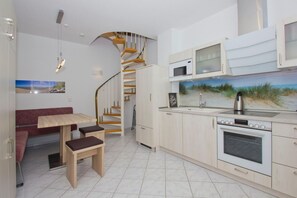 A modern kitchen with a built-in oven, microwave, and a painting of a beach scene. There is a dining area with a bench and a table.