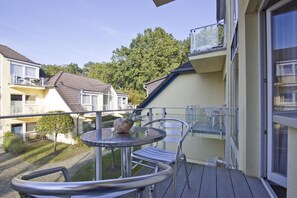 A balcony with a round table and chairs, a small decorative vase, and a view of neighboring buildings and trees. - Only 100 m to the beach, apartment with balcony and terrace - App. Eldena FeWo 04 - (Middelhagen)