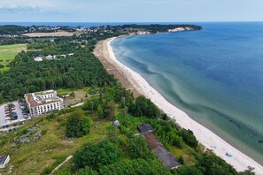 An aerial view of a coastal area with a beach, a large building with multiple floors, and a parking lot. - Only 100 m to the beach, apartment with balcony and terrace - App. Eldena FeWo 04 - (Middelhagen)
