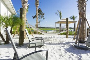 Relax on the beach with lounge chairs and a hammock, surrounded by lush greenery and a clear ocean view.