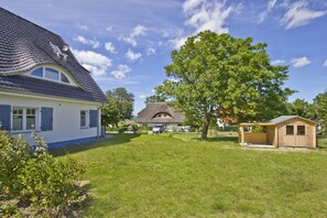 A house with a blue exterior, a thatched-roof structure in the background, a wooden shed, and a large tree in the front yard. - Vacation home Milan - waterfront vacation home with fireplace, sea view and garden - (Gager)