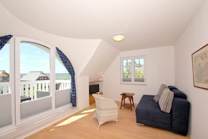 A spacious room with a large sliding glass door, a dark blue sofa, a white wicker chair, and a small wooden table. - Vacation Home in Milan - Waterfront vacation home with a fireplace, ocean view, and garden - (Gager)