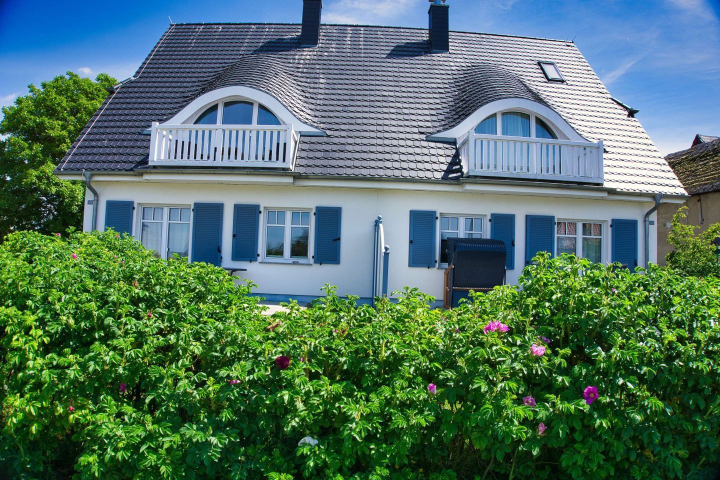 Una casa de dos plantas con techo a dos aguas, paredes exteriores blancas y contraventanas azules.