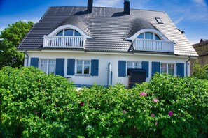 Una casa de dos plantas con techo a dos aguas, paredes exteriores blancas y contraventanas azules.