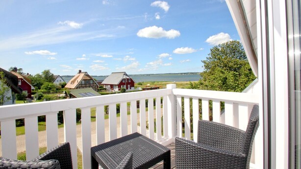 A balcony with wicker furniture, a white railing, and a view of houses and water. - Vacation home Milan - waterfront vacation home with fireplace, sea view and garden - (Gager)