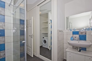 Une salle de bain moderne dotée d’une cabine de douche en verre, d’un lave-linge encastré et d’un lavabo avec miroir.
