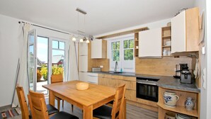 A modern kitchen with wooden cabinets, a dining table with chairs, and a view through a glass door to the outside. - Vacation home Milan - waterfront vacation home with fireplace, sea view and garden - (Gager)