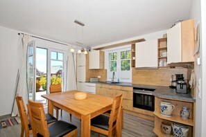 Una cocina moderna con armarios de madera, una mesa de comedor con sillas y vistas al exterior a través de una puerta de cristal.