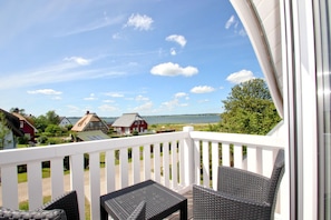 A balcony with wicker furniture, a white railing, and a view of houses and water.