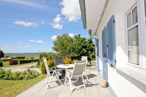 A patio with a table and chairs, a view of a body of water, and a house with blue shutters. - Vacation home Milan - waterfront vacation home with fireplace, sea view and garden - (Gager)