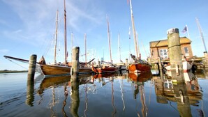 A calm harbor with several boats docked at wooden piers, a clear sky, and a building with a flag. - Vacation home Milan - waterfront vacation home with fireplace, sea view and garden - (Gager)
