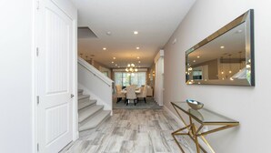 A modern interior with a staircase leading to a dining area, a glass console table, and a large mirror on the wall. - Family Escape With Private Pool & Themed Rooms (Kissimmee)