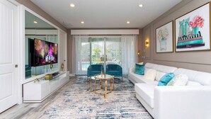 A modern living room with a flat-screen TV, two blue chairs, a white sofa with blue and white cushions, and a patterned rug. - Family Escape With Private Pool & Themed Rooms (Kissimmee)