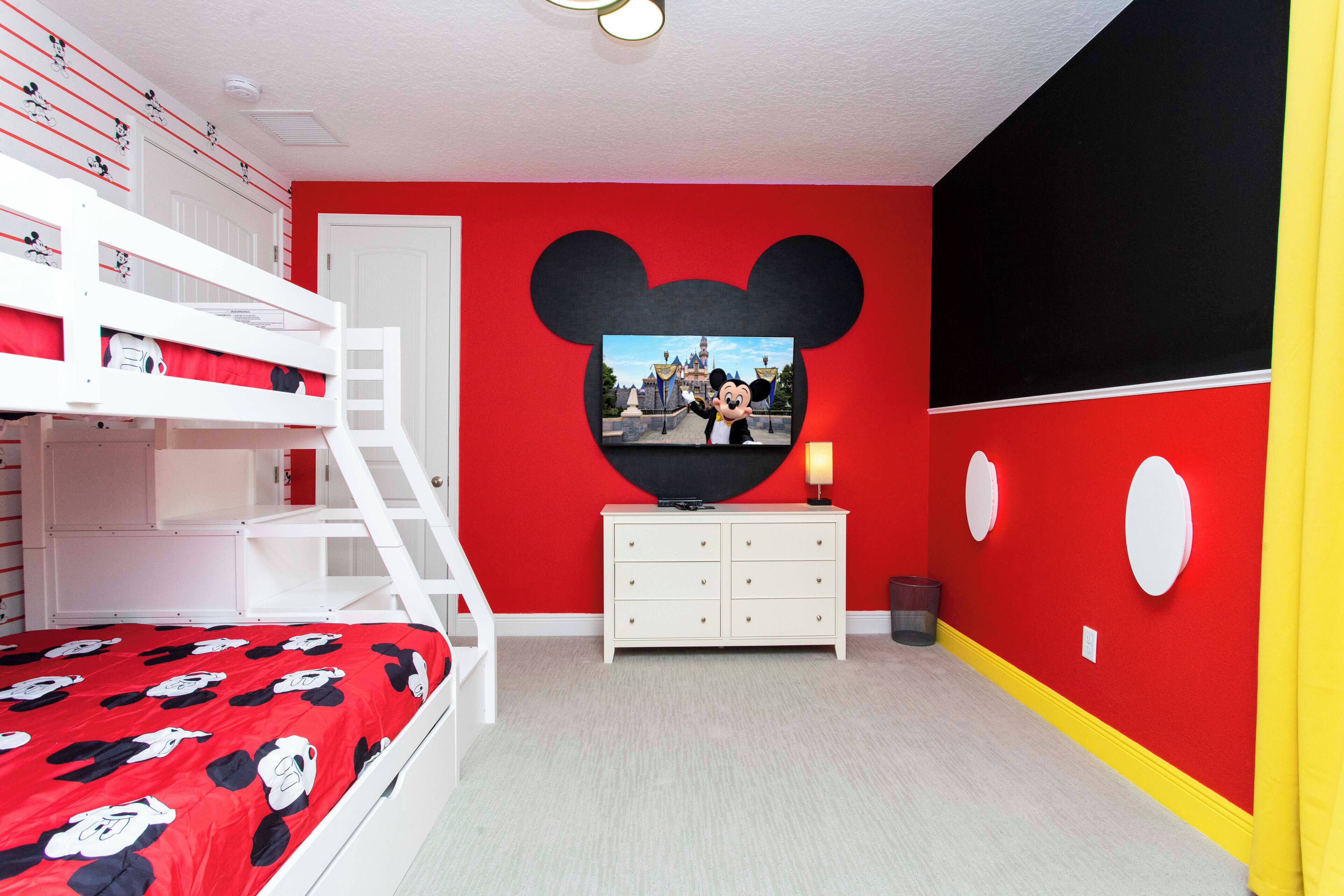 A room with a bunk bed, a dresser, and a wall with a large Mickey Mouse cutout.