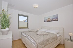Une chambre à coucher avec un lit, une fenêtre, un radiateur, une plante en pot, un tableau et des lampes de chevet.